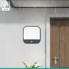 An outdoor wall lamp with a motion sensor is shown mounted on a white wall during a rain shower, next to a wooden door. Produktbild-Vorschau