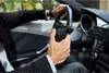 A person in a suit driving a car and holding a black thermos. Podgląd zdjęcia produktu