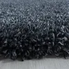 A close-up, low-angle view of a dark gray shaggy rug with a light gray wooden floor visible at the bottom. Produktbild-Vorschau