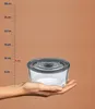 A hand holding a glass food container next to a ruler indicating measurements. Anteprima dell’immagine prodotto