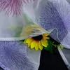 A close-up of a sunflower peeking through a sheer curtain with a floral pattern. Produktbild-Vorschau