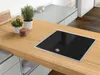 A modern kitchen countertop featuring an electric hob, two potted plants, and a wooden cutting board. Náhled obrázku produktu