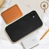 A black iPhone case, a brown leather card holder, and a white power bank are arranged on a white surface. Produktbild-Vorschau