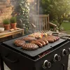 A barbecue grill with food cooking on it, set in an outdoor garden setting with a wooden bench and brick wall in the background. Náhľad obrázku produktu
