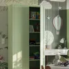 A child's bedroom with a light green metal cabinet, a desk with a lamp and a teddy bear, and decorative wall art. Anteprima dell’immagine prodotto