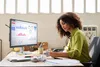 A woman is working at a desk with a computer monitor displaying charts and graphs. Voir les images du produit