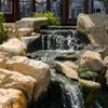 A close-up view of a man-made waterfall in a garden setting, with rocks and flowing water. Produktbild-Vorschau