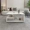 A modern living room scene with a white coffee table in the foreground and a sectional sofa in the background. Náhled obrázku produktu
