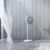 A white standing fan is placed on a tiled floor in front of a textured gray wall, with sheer white curtains on the left side. Anteprima dell’immagine prodotto