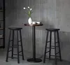 Two black bar stools are placed on either side of a tall, round-top table in a room with a gray, textured wall. Produktbild-Vorschau
