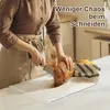 A person is cutting bread on a transparent cutting board with a lip. Produktbild-Vorschau