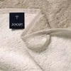 A close-up view of a beige towel with a black label that says JOOP! and a small umbrella logo. Produktbild-Vorschau