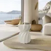 A stylish living room with a view of the sea, featuring a white textured side table with books and a vase. Anteprima dell’immagine prodotto