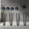 Four black hairpin legs and four gray protective caps are displayed on a light gray and white surface with a blurred background. Podgląd zdjęcia produktu