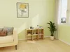 A living room scene with a couch, a cube shelf filled with books and decor, and a large plant near a window. Produktbild-Vorschau