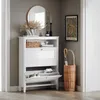 A white shoe cabinet with slatted doors and open shelves, next to a wicker umbrella stand. Anteprima dell’immagine prodotto