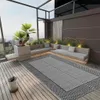 A modern outdoor patio with a rug, seating, and plants. Produktbild-Vorschau