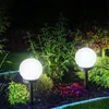 Two white globe-shaped solar lights illuminate a garden at night. Produktbild-Vorschau