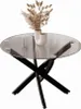 A round glass-top coffee table with a black crisscross base, decorated with a vase of dried flowers. Produktbild-Vorschau
