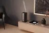 A dark humidifier is shown emitting mist on a wooden cabinet next to books and a vase. Náhľad obrázku produktu