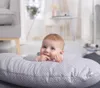 A baby is lying on a polka-dot pillow in a living room. Produktbild-Vorschau