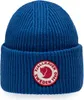 A blue knitted beanie with a circular red and white logo patch on the front. Produktbild-Vorschau