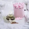 A perfume bottle and a box of roses on a white fabric background. Voir les images du produit