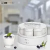 A yogurt maker with a glass of yogurt and blueberries on a white surface, with a blurred kitchen background. Produktbild-Vorschau