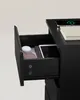 A partially opened drawer of a black nightstand with items inside, and a smartphone with wireless charging indicator on top. Náhled obrázku produktu