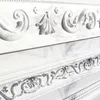 Close-up view of ornate white decorative molding with intricate patterns and details, set against a marble-like background. Produktbild-Vorschau