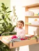 A baby sitting on a wall-mounted changing table with shelves above. Produktbild-Vorschau