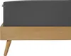 A close-up view of a dark gray fitted sheet on a wooden bed frame with angled legs. Produktbild-Vorschau