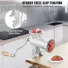A manual meat grinder is shown on a wooden table in a kitchen setting, with raw meat in the grinder and ground meat on a plate. Náhľad obrázku produktu