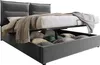 A grey upholstered bed frame with the mattress lifted to reveal storage space underneath, filled with pillows. Podgląd zdjęcia produktu