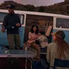 People gathered around a van with a table set up for a picnic. Produktbild-Vorschau