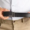 A person is holding a black leather belt with a silver buckle, showing the buckle mechanism. Anteprima dell’immagine prodotto