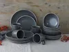 A collection of dark gray speckled stoneware dinnerware, including plates, bowls, and mugs, arranged on a light-colored tablecloth against a wooden background. Náhľad obrázku produktu