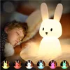 A child sleeping next to a glowing bunny-shaped night light on a table. Produktbild-Vorschau