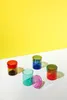 Five colorful glass jars are arranged on a white surface against a bright yellow background. Produktbild-Vorschau