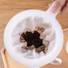 A hand holding a coffee filter with used coffee grounds inside, placed on a wooden tray. Produktbild-Vorschau