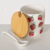 A ceramic jar with a strawberry pattern, a wooden lid, and a white spoon. Produktbild-Vorschau