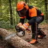 A person wearing safety gear is using a chainsaw to cut a log in a forest. Produktbild-Vorschau