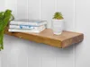 A wooden shelf mounted on a white paneled wall, with books and a decorative plant pot on it. Produktbild-Vorschau