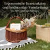 A picnic basket filled with decorative items and a book, placed on a blanket on the grass next to a wooden crate with grapes and a bottle. Náhľad obrázku produktu