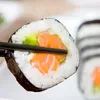 A close-up shot of a sushi roll being held by chopsticks. Voir les images du produit