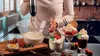 A person is using a hand blender to mix ingredients in a bowl, with several ice cream desserts and berries on a table in the foreground. Anteprima dell’immagine prodotto