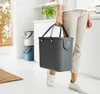 A person is carrying a gray trash bin with handles in a modern kitchen or utility room. Other trash bins are visible in the background. Produktbild-Vorschau