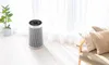 An air purifier is placed in a bright room next to a window with sheer curtains. A potted plant is on the left, and a chair with cushions is on the right. Anteprima dell’immagine prodotto