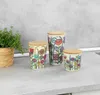 Three decorative storage jars with bamboo lids are arranged on a countertop next to a potted plant. Produktbild-Vorschau