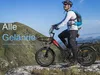 A man riding an electric fat tire bike on a rocky, mountainous terrain with a clear blue sky. Produktbild-Vorschau